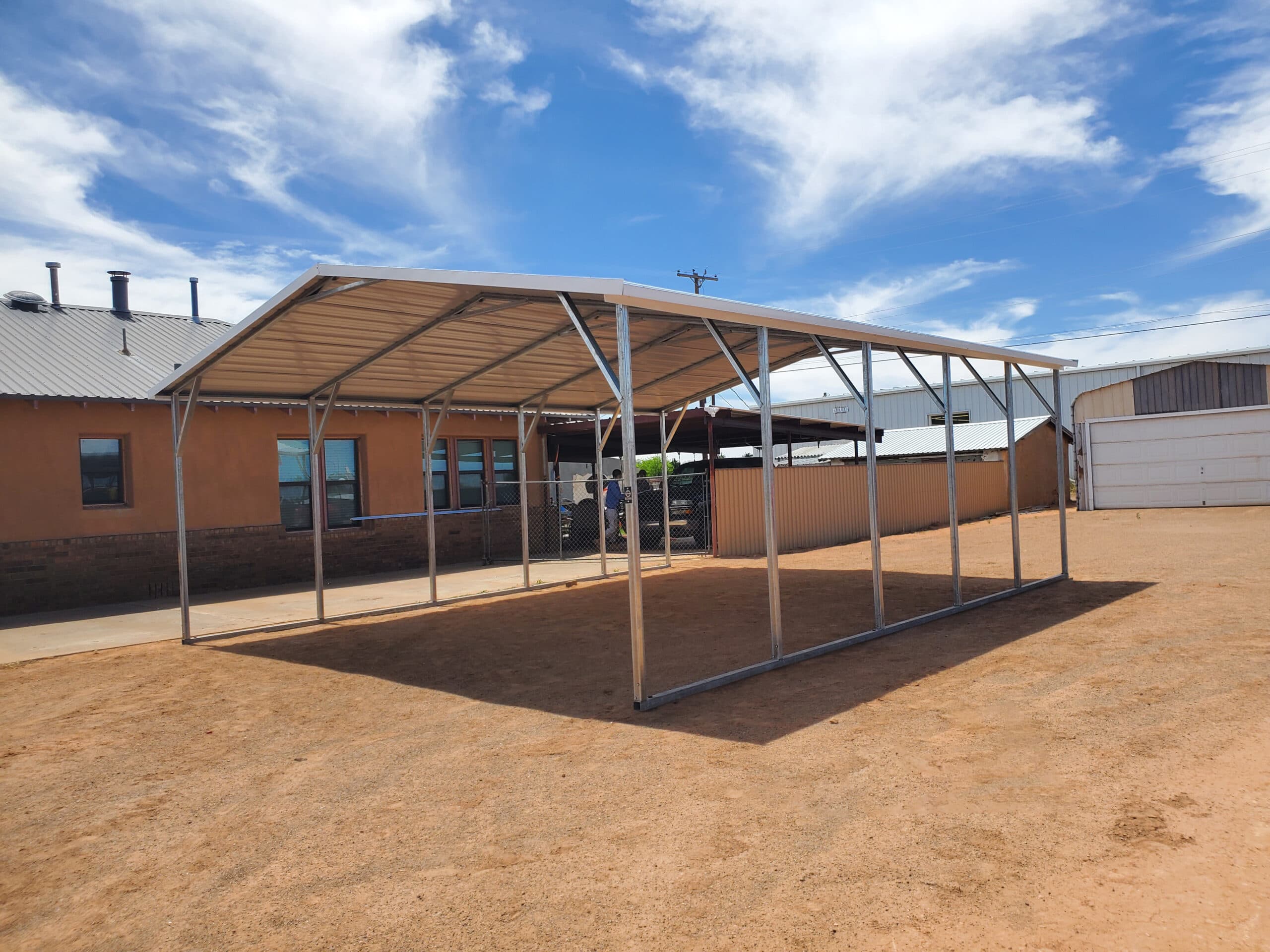 A wide steel carport with a horizontal-panel roof over farm equipment