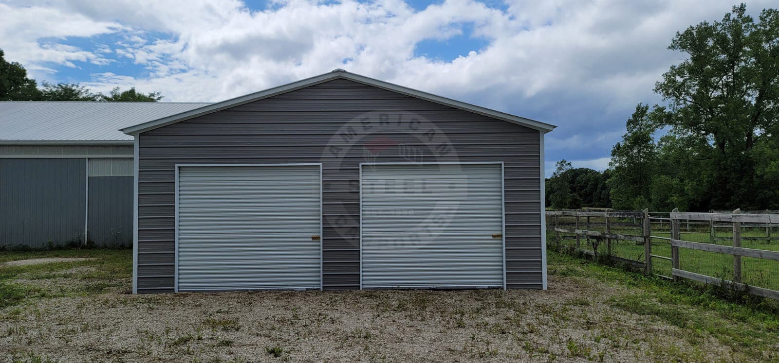 A two-car American Steel metal garage with two roll-up doors, installed on a gravel pad